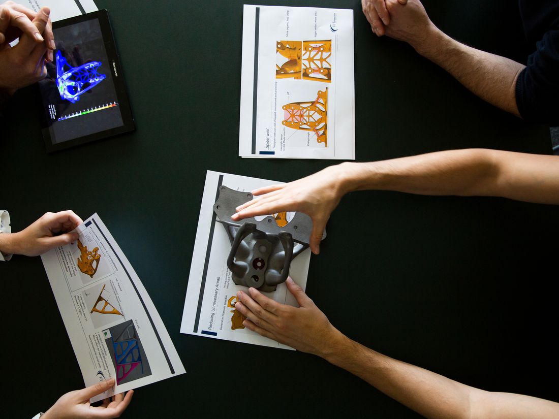 Besprechung am Tisch mit Zeichnungen, Tablet und einem Metallbauteil